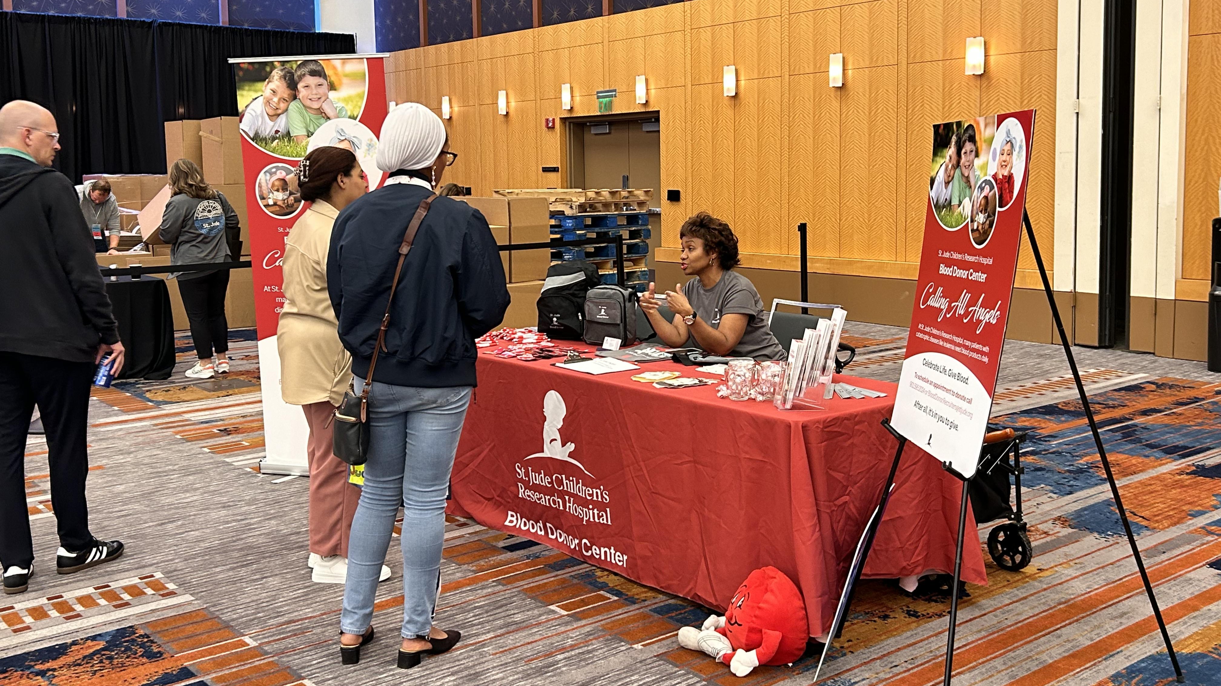 Image showing people interacting with St. Jude Blood Donor Center Recruiter at a booth.